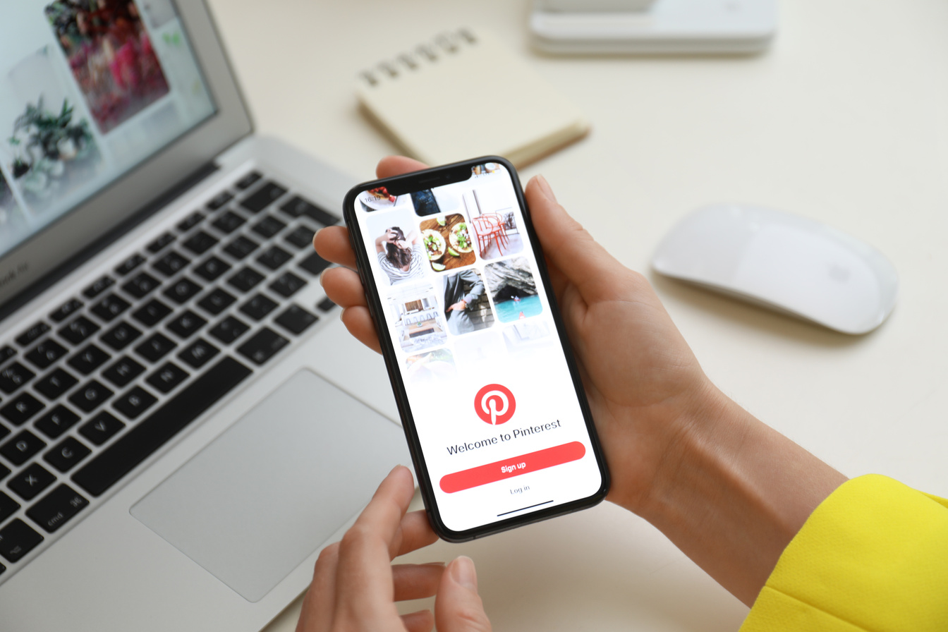 MYKOLAIV, UKRAINE - AUGUST 28, 2020: Woman Holding IPhone 11 with Pinterest App on Screen at Table, Closeup